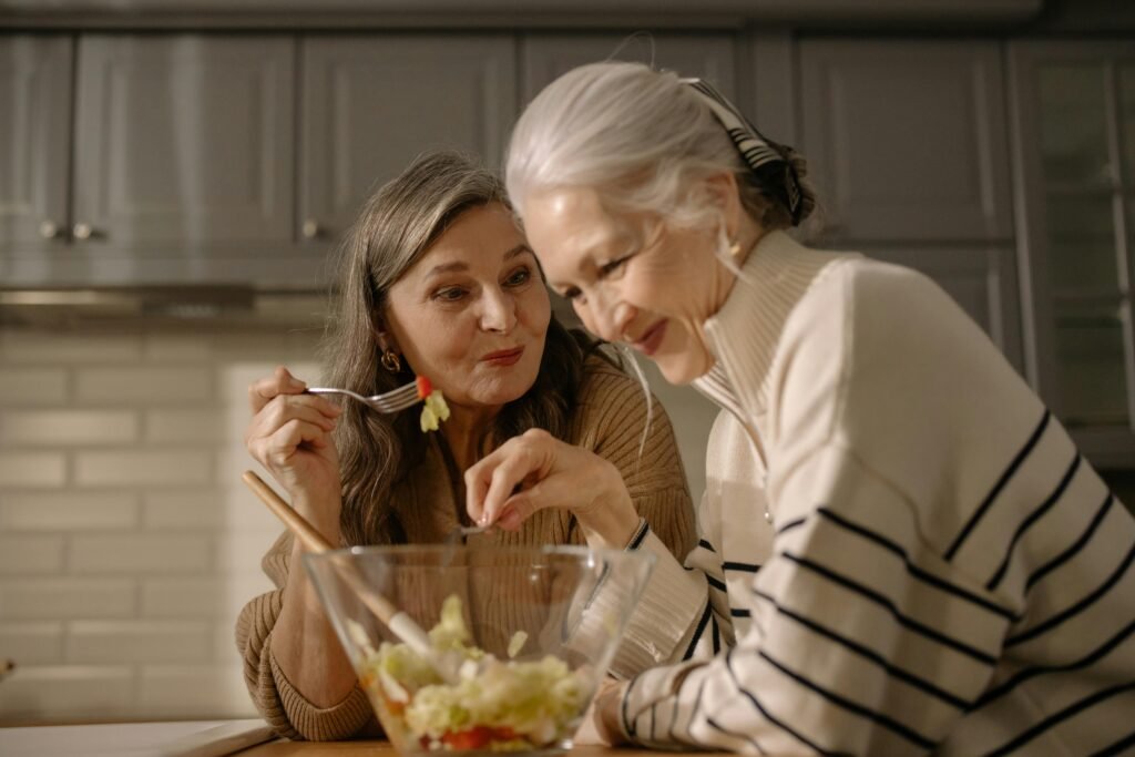 Two women enjoying a fresh salad in a sustainable kitchen setting.